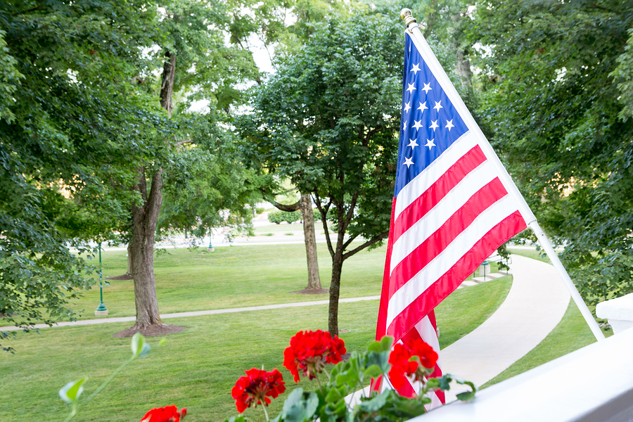 American Flag Flying From A Balcony Or Patio Among Flowers And A Beautiful Lawn.