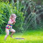 Little girl playing in the spray of a sprinkler