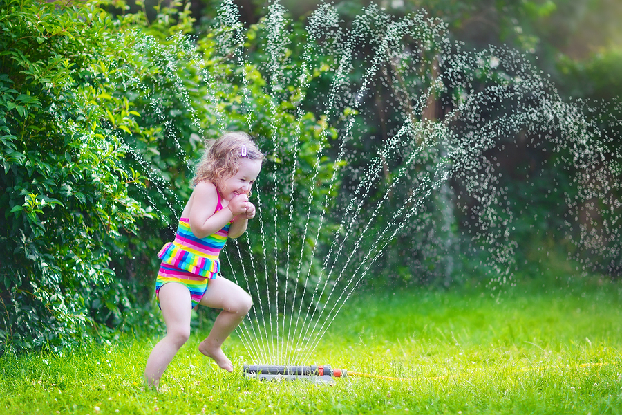 Little girl playing in the spray of a sprinkler